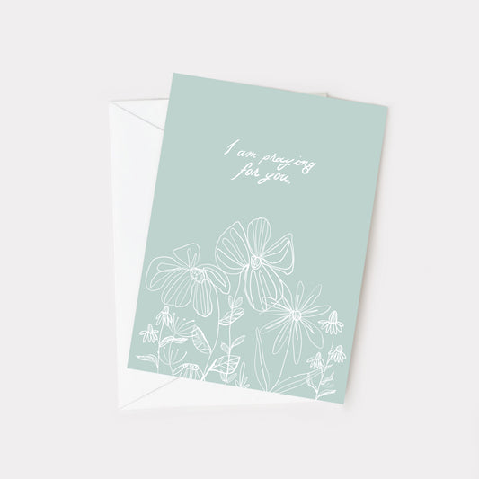 light teal greeting card with ehite floral line art. Text reads I am praying for you. 